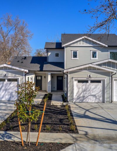 A modern duplex with two garages and separate entrances, surrounded by a newly landscaped yard on a clear day.