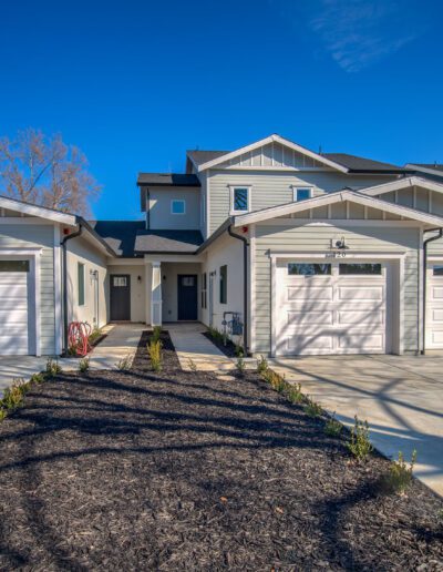 Duplex with two garages, white and gray exterior, and a shared driveway under a clear blue sky.