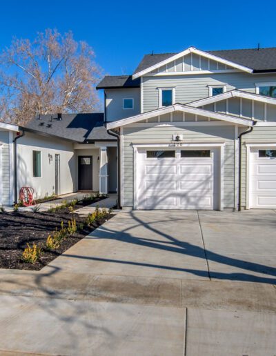 A modern two-story house with a driveway and three garages, featuring light gray siding and a manicured front yard.