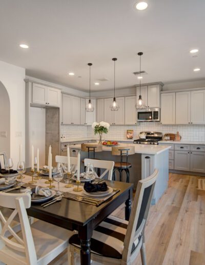 Modern kitchen and dining area with wooden floors, gray cabinets, an island with pendant lighting, and a table set for six.