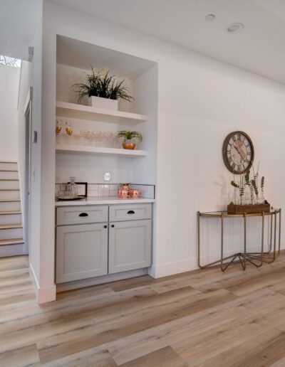 Modern hallway with light wood flooring, a built-in shelving unit, and a staircase on the left. A large clock hangs above a console table on the right.