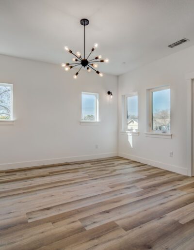 An empty room with light wood flooring, white walls, modern light fixture, three windows, and an open door leading to a bathroom.