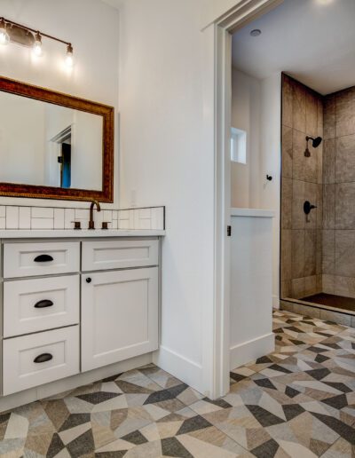 Bathroom with white cabinetry, patterned floor, large mirror, and a walk-in shower with tiled walls.