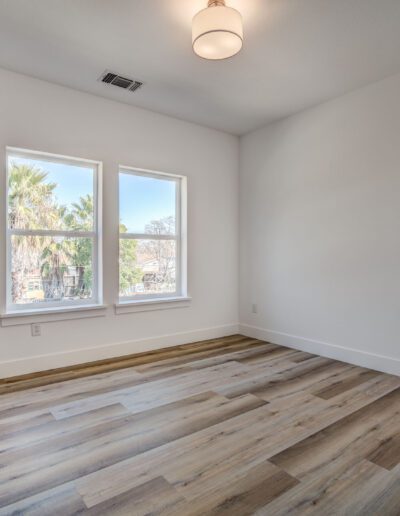 Unfurnished room with light wood flooring, white walls, two windows, a modern light fixture, and a black door.