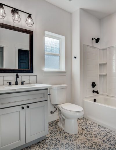 A modern bathroom with a white vanity, black fixtures, a rectangular mirror, a bathtub-shower combo, and patterned floor tiles.