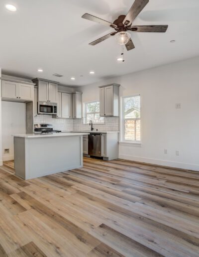 Open-concept kitchen with white cabinets and center island, wood flooring, ceiling fan, and natural light from multiple windows.