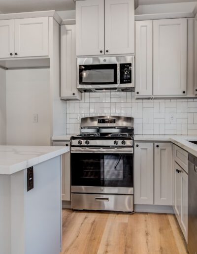 Modern kitchen with white cabinets, stainless steel appliances, and light wood flooring. Features a gas stove, microwave, dishwasher, and white tile backsplash.