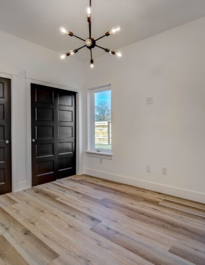 Empty room with light wood flooring, white walls, two windows, dark double doors, and a modern black ceiling light fixture.