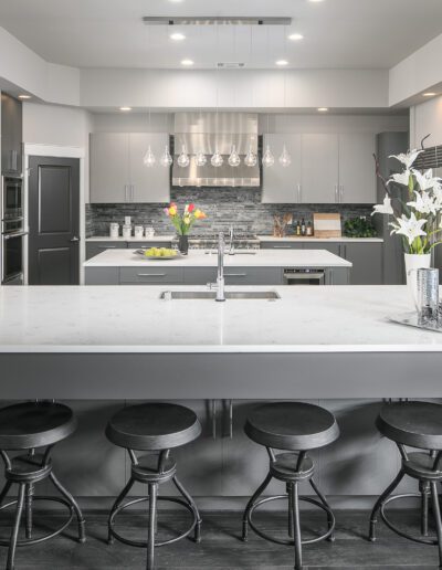 Modern kitchen with a large island, bar stools, stainless steel appliances, and decorative flowers.