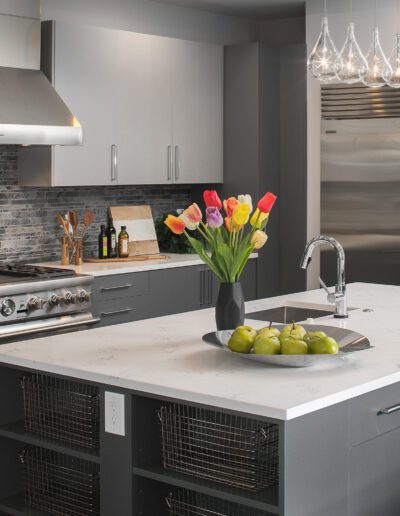 Modern kitchen with a large island, stainless steel appliances, and a vase of colorful tulips on the countertop. A bowl with green apples is also on the island.