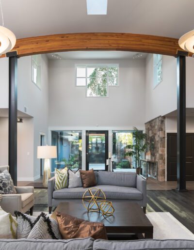 Spacious modern living room with high ceilings, contemporary furniture, and large windows. Features wooden ceiling beams, stylish light fixtures, and a view of an outdoor area.