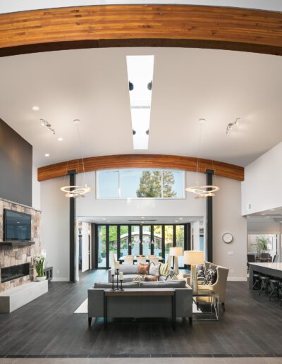 Spacious modern living room with wooden arches, large windows, contemporary furniture, stone fireplace, and overhead lighting.