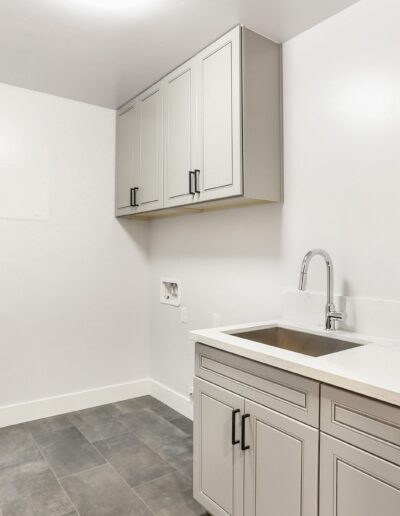 A modern laundry room with gray cabinets, a countertop with a sink, and a tile floor.