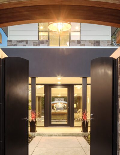 Modern house entrance with stone pillars and open double doors leading to a well-lit interior.