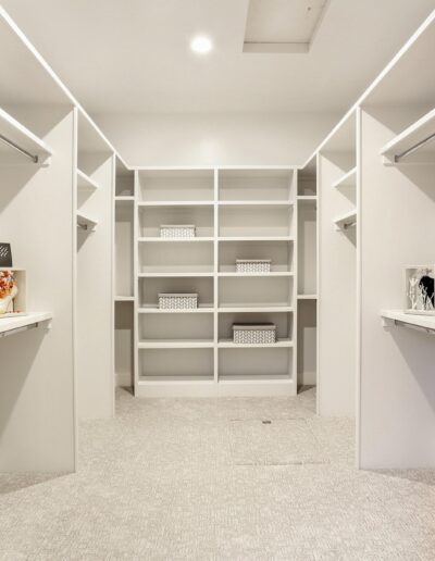 Spacious, empty walk-in closet with white shelves and carpeted floor.