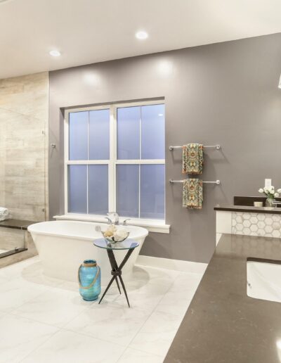 Modern bathroom with a freestanding tub, glass shower, double sinks, large mirror, and decorative accents on the countertops and walls.