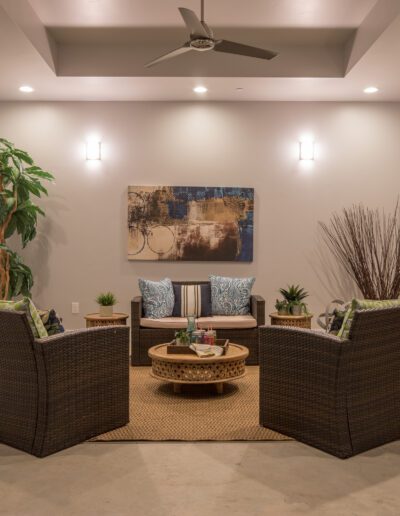 Cozy patio with wicker chairs around a round table, a stone fireplace, indoor plants, abstract wall art, and a ceiling fan.