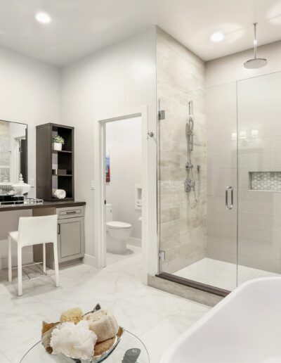 Modern bathroom with glass shower, double vanity, backlit mirrors, and white freestanding tub. Tiled flooring and neutral color scheme create a sleek, minimalist design.