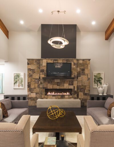 Spacious modern living room with a central fireplace, wall-mounted TV, contemporary furniture, and soft lighting.