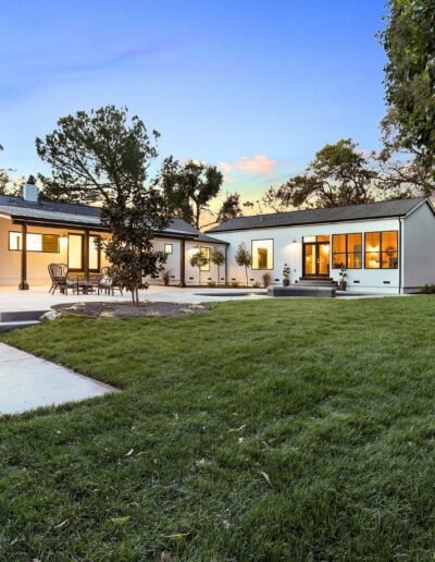 Modern house with large windows and a spacious backyard featuring a patio and green lawn at dusk.