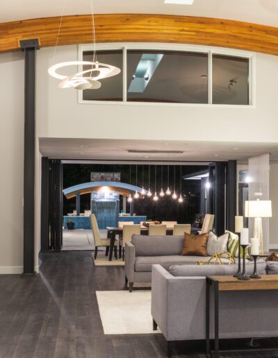 Modern living room with gray sofas, stone fireplace, and circular light fixtures. Glass doors open to a patio with pool.