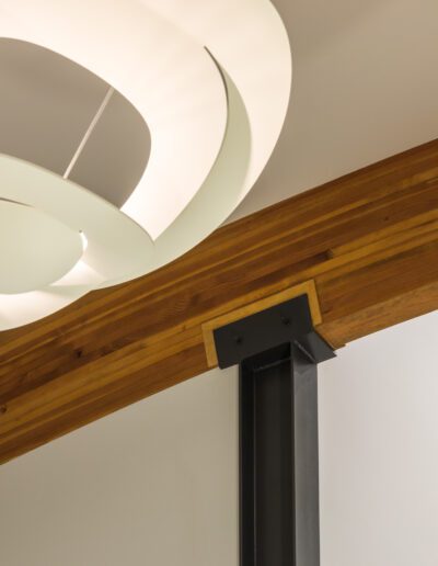 Modern ceiling with a white abstract light fixture and a wooden architectural beam, leading to a large window with white walls.