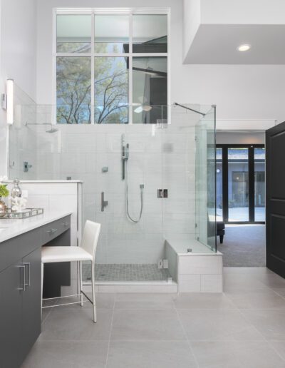 Spacious modern bathroom with glass shower, black cabinets, white countertops, and large windows.