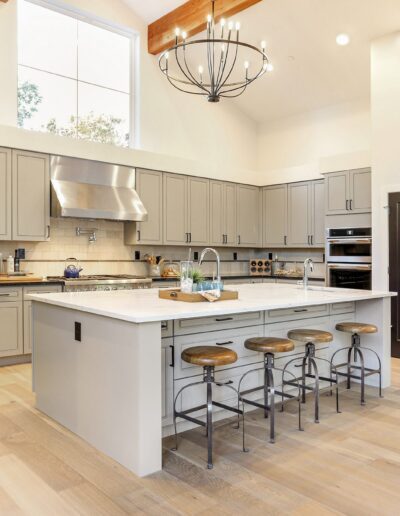 Spacious kitchen with high ceilings, an island with stools, light wood flooring, gray cabinetry, and a large chandelier.