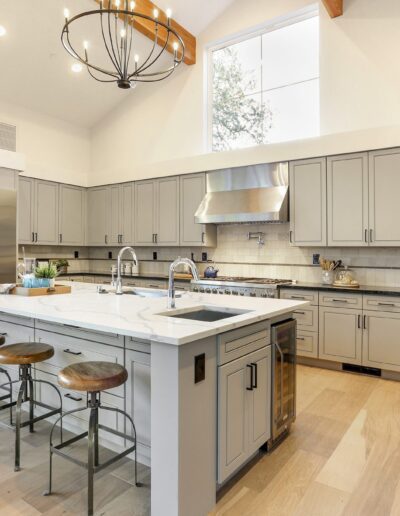 Spacious kitchen with gray cabinets, a large island with wood bar stools, stainless steel appliances, and a high ceiling with a modern chandelier.