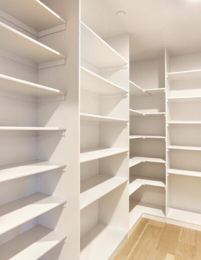 Empty walk-in pantry with white shelves and wooden floors.