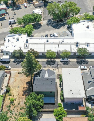 Aerial view of a residential neighborhood with a row of houses and a commercial building. Cars are parked along the street, and trees are scattered throughout the area.