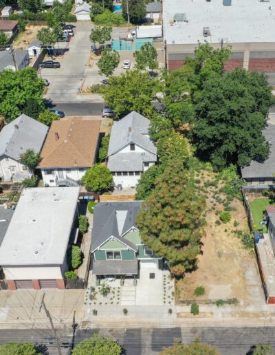 Aerial view of a residential neighborhood with houses, trees, and a large white-roofed building in the background.