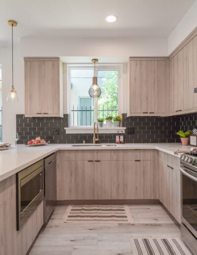 Modern kitchen with wooden cabinets, black tile backsplash, and stainless steel appliances. Pendant lights hang over a white island with an integrated stovetop and oven.