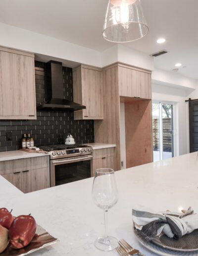 Modern kitchen with wooden cabinets, black backsplash, and a white countertop. Glasses, pears, and napkins are on the island. Pendant lights hang above.