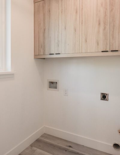 Empty laundry room with wooden cabinets, a window on the left, and connections for a washer and dryer.