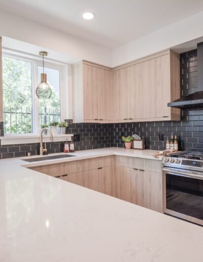 Modern kitchen with light wood cabinets, black subway tile backsplash, stainless steel appliances, and pendant lighting over a white marble island.