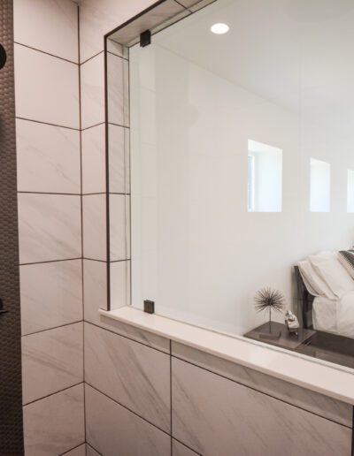 View of a bedroom through a glass wall from a tiled bathroom with a modern shower.